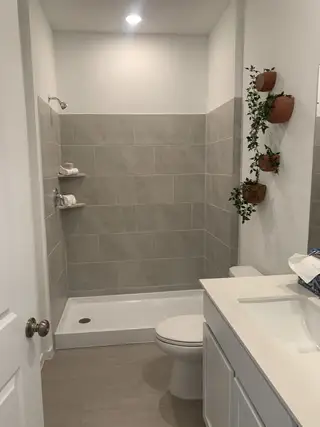 A modern bathroom with large gray tiles, floating shelves, and sleek white vanity, complemented by decorative wall planters.