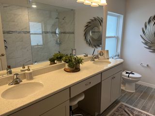 Model Home A modern bathroom with a glass-enclosed shower, dual sinks, decorative mirrors, and elegant plants adding a touch of greenery.