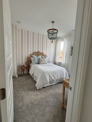 A cozy bedroom with striped wallpaper, a rattan headboard, plush bedding, and a chic beaded chandelier.