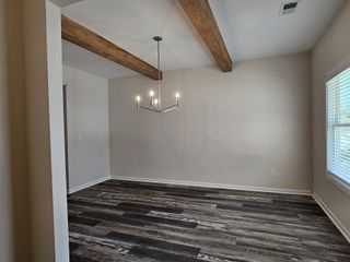 Open dining area with wooden ceiling beams, chandelier lighting, and modern dark-toned flooring.