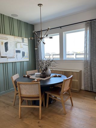 A modern dining area with a round table, stylish chairs, green accent wall, and chic lighting fixture.