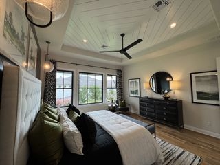 A cozy bedroom featuring a tufted headboard, wooden flooring, decorative mirrors, and large windows for natural light.