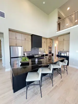Model Home A modern kitchen with high ceilings, light wood cabinetry, a sleek black island, and stylish seating.