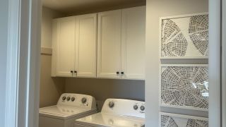 A practical laundry room with sleek white cabinets, modern appliances, and decorative wall art.