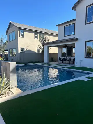 Model Home A luxurious backyard with a modern pool, artificial grass, and a covered patio area for outdoor dining.