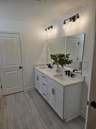 A sleek bathroom featuring a dual-sink white vanity, elegant lighting, and modern tile flooring.