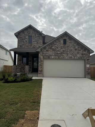 A charming two-story brick home with a lush lawn in The Parklands by Coventry Homes (Schertz, TX).