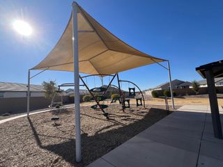 Community Amenities A charming shaded playground in Tortosa by D.R. Horton, Maricopa, AZ, featuring swings and surrounded by a serene landscape.