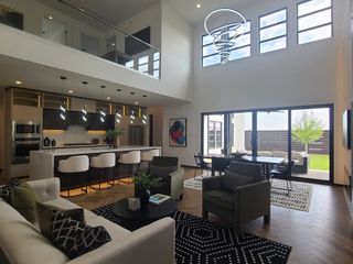 A modern living area with high ceilings, sleek kitchen, stylish lighting, and large windows opening to a patio.