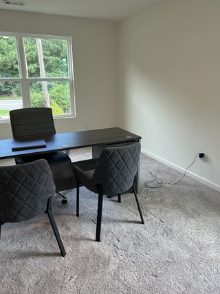 A bright office space with a sleek desk, modern chairs, and plush carpeting, featuring large windows with a view.