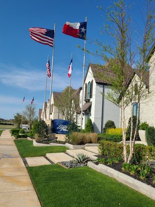 A charming home with lush landscaping and flags in Star Trail - 65s by American Legend Homes (Prosper, TX).