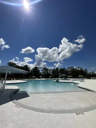 Sunlit pool with umbrellas and chairs in Carolina Groves Townhomes by D.R. Horton, Moncks Corner, SC.