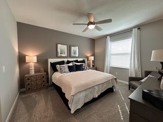 A peaceful primary suite with a ceiling fan, plush carpeting, and warm lighting.