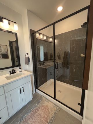 A stylish bathroom with a double vanity, sleek black fixtures, and a tiled shower in Solterra Texas by Cadence Homes (Mesquite, TX).