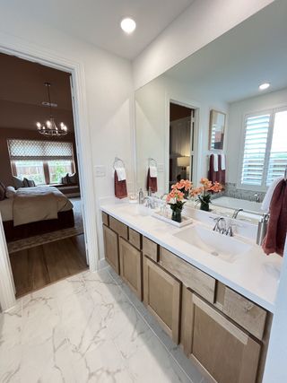 A modern bathroom featuring a spacious vanity, elegant marble flooring, and a view into a cozy, well-lit bedroom.