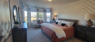 A cozy bedroom with a chevron accent wall, large windows, and warm bedding, paired with stylish furnishings.