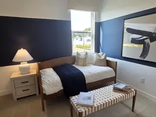 A cozy bedroom featuring a daybed, modern art, a sleek lamp, and a large window for natural light.