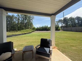 Model Home A cozy covered patio with outdoor seating overlooking a spacious, well-maintained lawn.