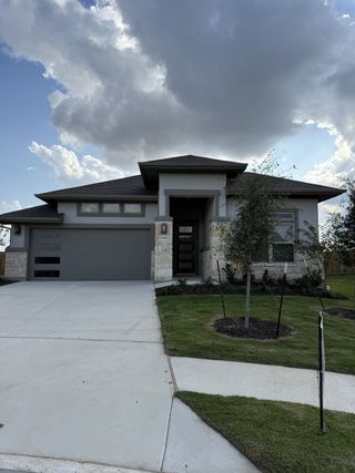Street view Modern stone-accented home with a sleek exterior and manicured lawn in Carillon by Brightland Homes (Manor, TX).