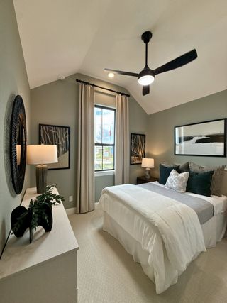 A cozy bedroom with soft green walls, elegant bedding, modern art, and a sleek ceiling fan.