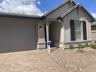A charming single-story home features neutral siding, dark shutters, a paved driveway, and desert landscaping in The Villas at Mystic by Brightland Homes (Peoria, AZ).
