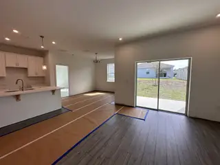 An open living area with sliding glass doors, wood flooring, and a modern kitchen featuring white cabinetry and pendant lighting.