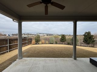 Model Home A spacious covered patio with ceiling fan and landscape view, ideal for relaxation in Emory Crossing by Taylor Morrison (Hutto, TX).