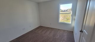 A bright bedroom with neutral walls, a large window, and plush carpeting. Perfect for personalization.