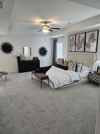 Model Home A spacious primary suite with neutral tones, elegant wall décor, and a stylish ceiling fan.