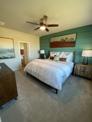 Model Home A cozy bedroom with a green accent wall, stylish art, wooden furniture, and a ceiling fan for comfort.