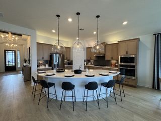 Model Home A modern kitchen with sleek wood cabinets, an elegant island with barstools, and chic pendant lighting.