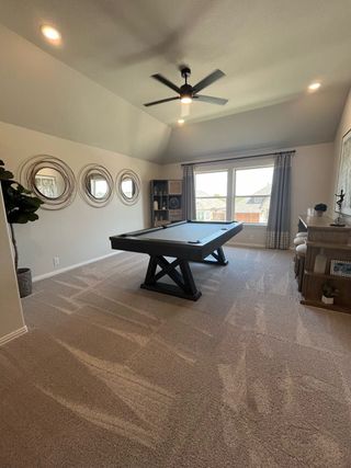 A spacious game room with plush carpeting, a sleek pool table, modern mirrors, and abundant natural light.
