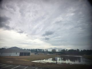 A picturesque home with a pond view in Creekside Landing by Maronda Homes, Callahan, FL, under a vast cloudy sky.