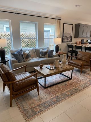 A cozy living area with modern leather chairs, a plush sofa, and a stylish rug. Open concept flows into the kitchen.