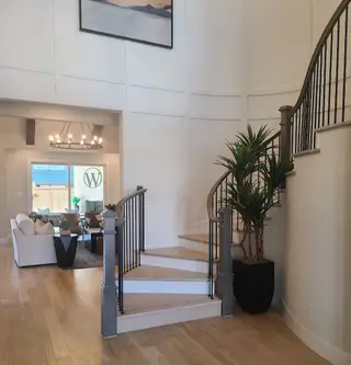 A welcoming foyer with elegant curved stairs, hardwood floors, and a cozy glimpse into the living room area.