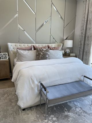 A luxurious bedroom featuring a tufted headboard, elegant geometric accent wall, and plush seating bench in soothing neutral tones.
