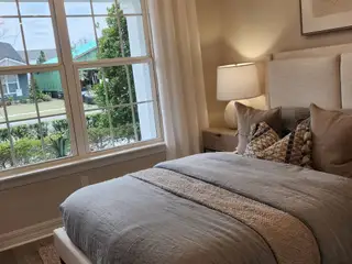 A beautifully designed master suite with a plush upholstered bed, warm neutral tones, and large windows offering serene views of the outdoors.