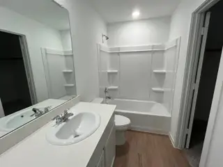 A sleek bathroom with a white vanity, spacious mirror, and a built-in tub with shelving for convenience.
