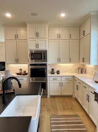 A modern kitchen with white cabinetry, black countertops, and hardwood flooring, featuring stainless steel appliances.
