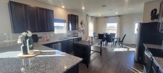 A modern kitchen with granite countertops, dark cabinetry, and an open dining area filled with natural light.