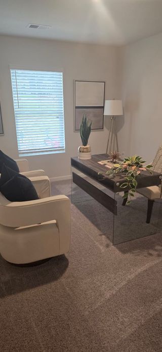 A cozy home office with a sleek glass desk, plush chairs, and stylish decor, bathed in natural light from a large window.