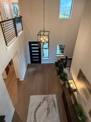 A modern entryway with wood flooring, elegant chandelier, and sleek railing, offering a spacious and inviting atmosphere.
