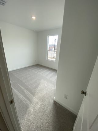 A bright room with fresh white walls, soft carpeting, and a large window bringing natural light into the space.