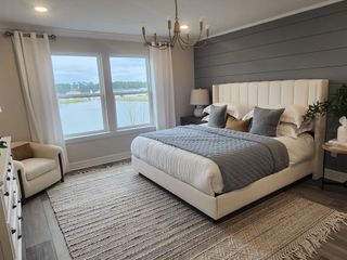 Model Home A luxurious master bedroom with a serene water view, plush bedding, a paneled accent wall, and elegant lighting.