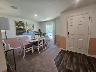 A cozy dining area with a white table set, tropical artwork, and natural light. Warm tones complement the wood-accented floor.