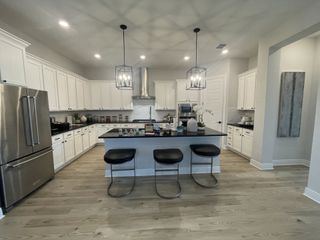 A spacious kitchen with white cabinetry, sleek stainless steel appliances, an island with bar stools, and modern pendant lights.
