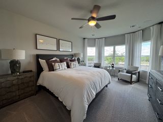 A serene bedroom with a plush bed, modern furniture, ceiling fan, and expansive windows offering a view of the outdoors.