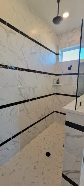 Model Home A modern shower featuring marble tile with sleek black accents and a rainfall showerhead.