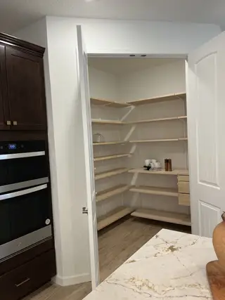Model Home A spacious kitchen pantry with open shelving, dark cabinetry, and a marble countertop for organized storage.