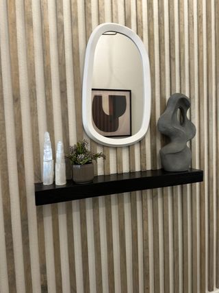 A chic wall design with vertical wood slats, modern mirror, and sleek shelf adorned with abstract decor and greenery.